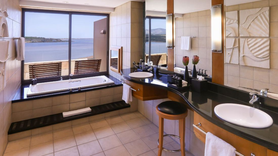 A bathroom with a bath beside a large window overlooking the water