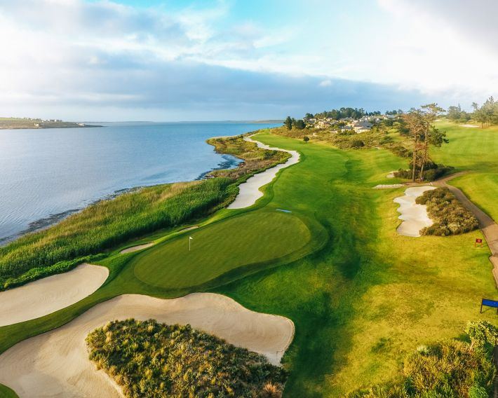 Golf fairways and white bunkers beside a wide lagoon
