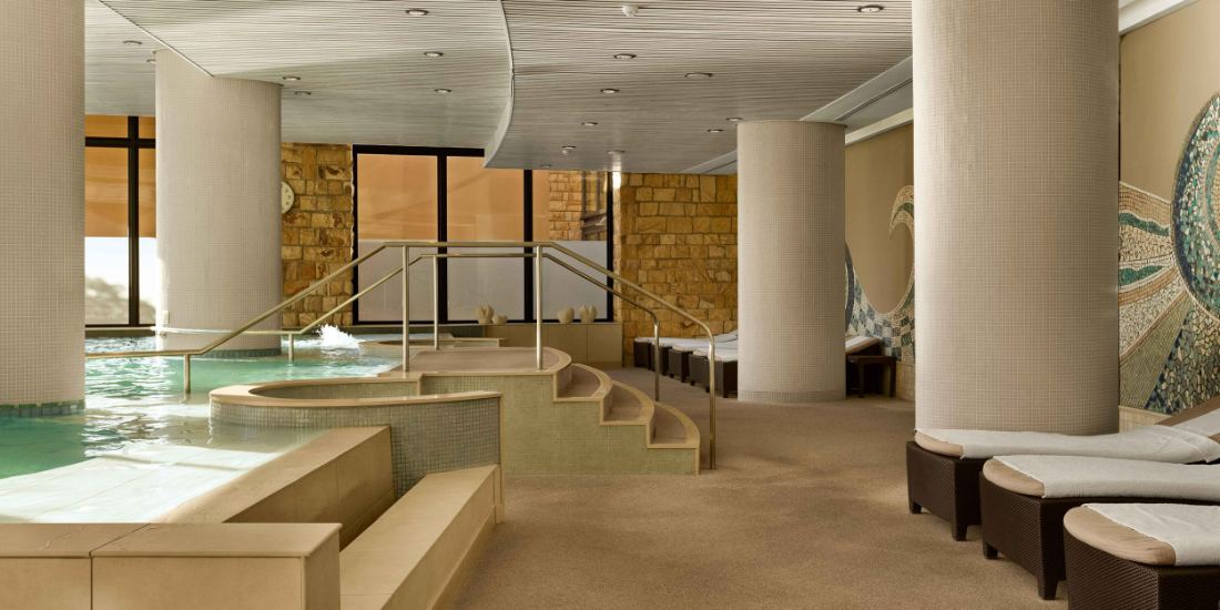 A calm indoor pool with loungers in a stone-walled spa