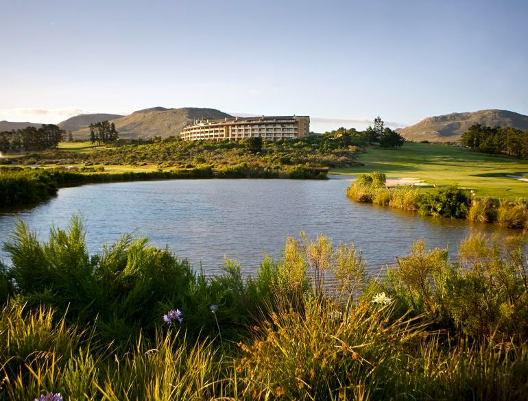 The long low hotel seen across a pond fringed with fynbos