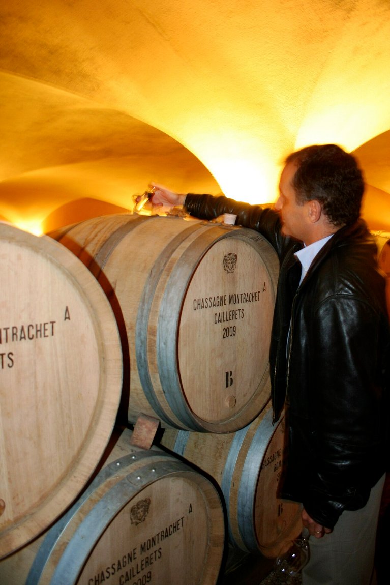 A winemaker drawing wine from an oak barrel in a cellar with a long glass pipette