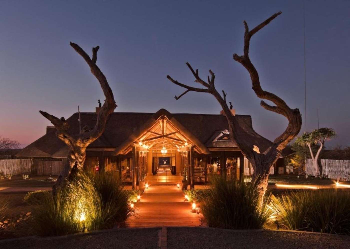 The lodge entrance lit up at dusk between two old dead trees