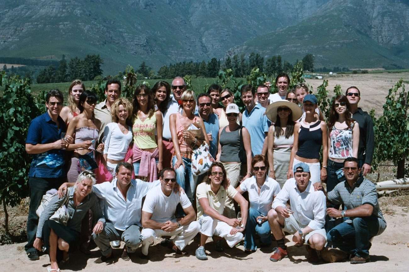 A group of about thirty guests in a vineyard with mountains behind