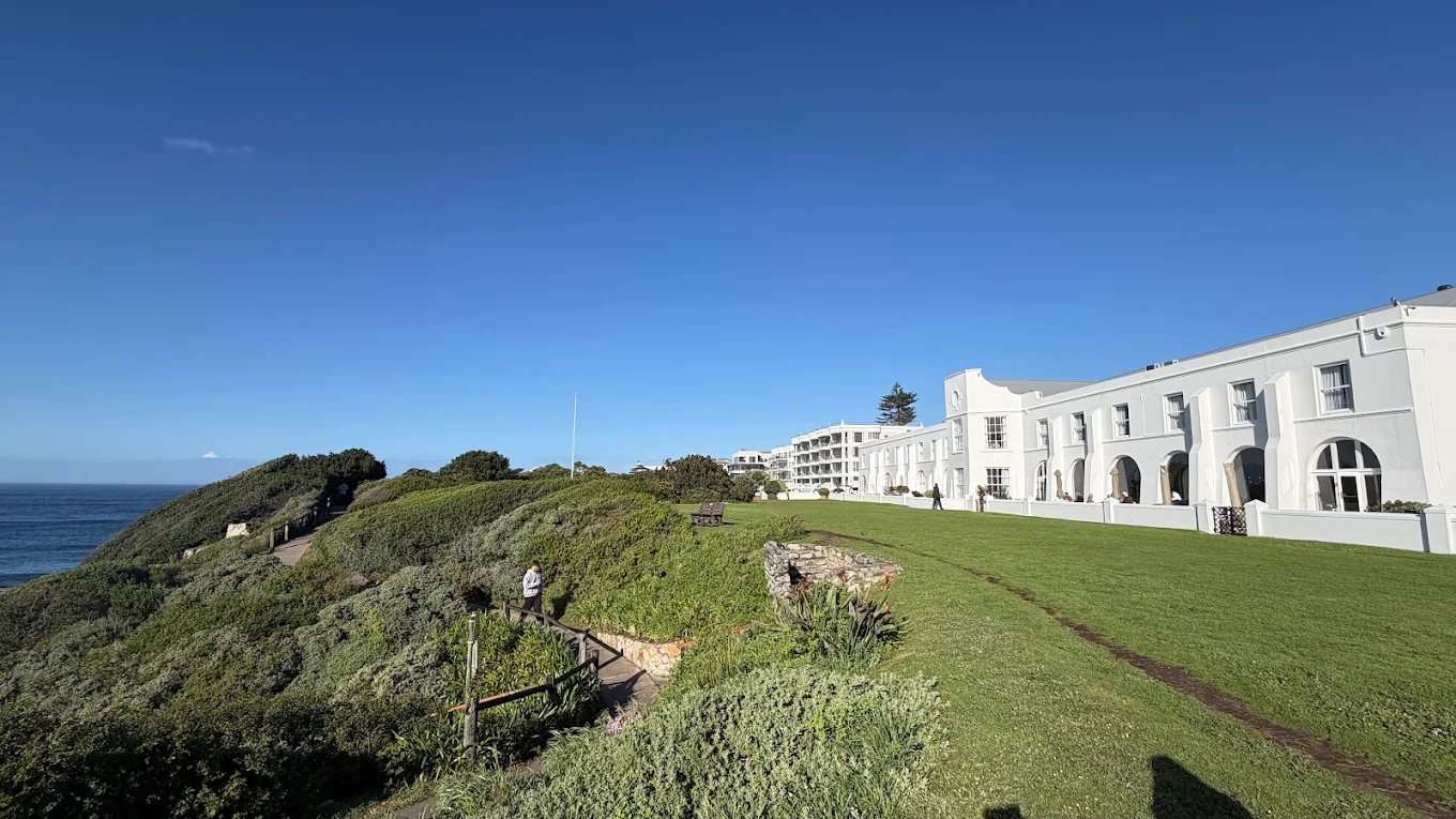 The Marine, white against a blue sky, with its lawn running to the cliff path and the sea