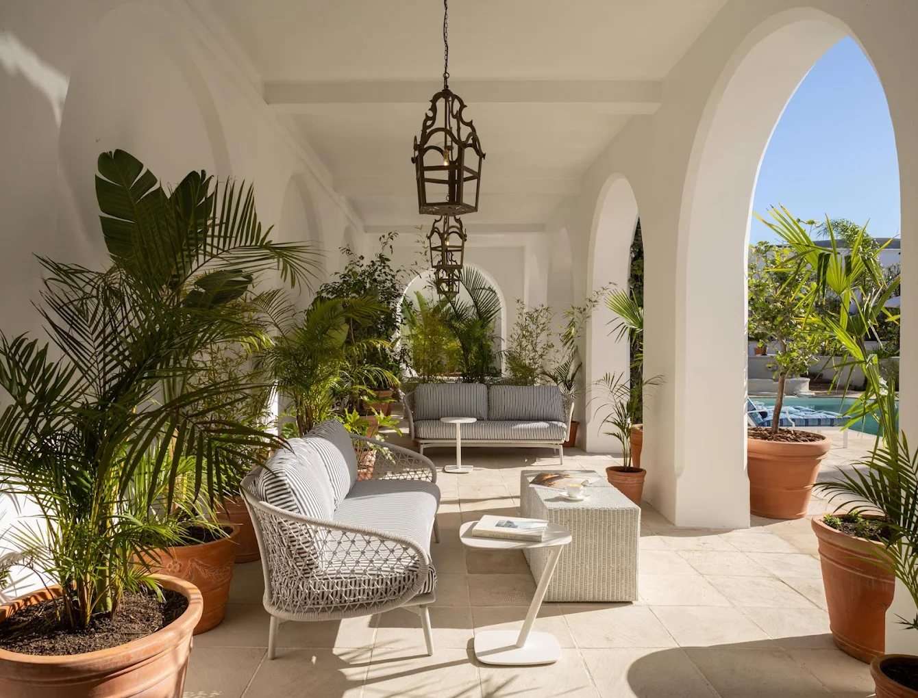 A white arched cloister with palms and lanterns, the pool beyond