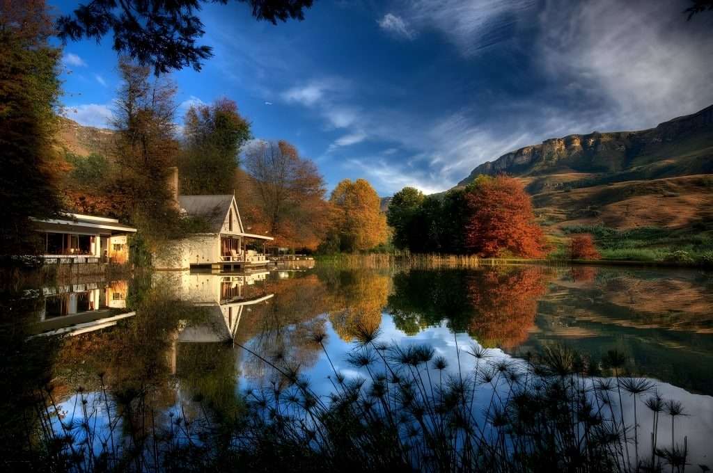 Cleopatra Mountain Farmhouse reflected in its trout dam in autumn, with the Drakensberg escarpment behind