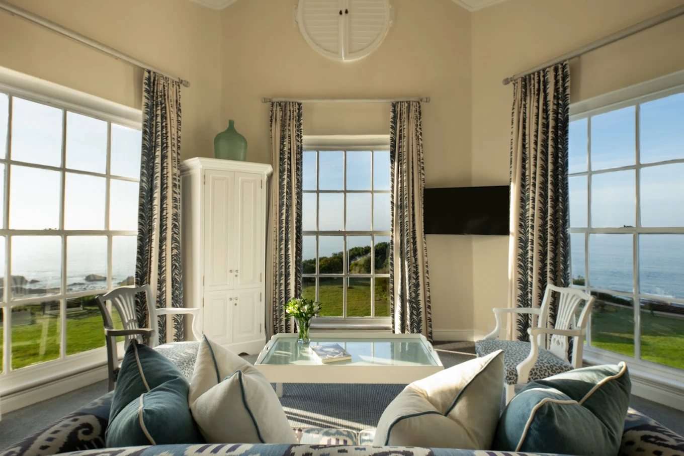 A light-filled suite lounge with tall windows onto the lawn and the sea