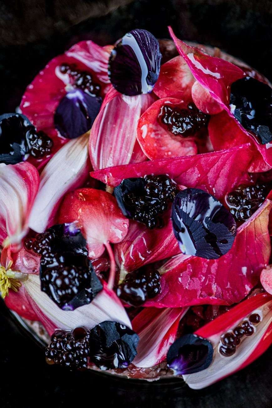 A dessert of red berries and cream on a dark plate