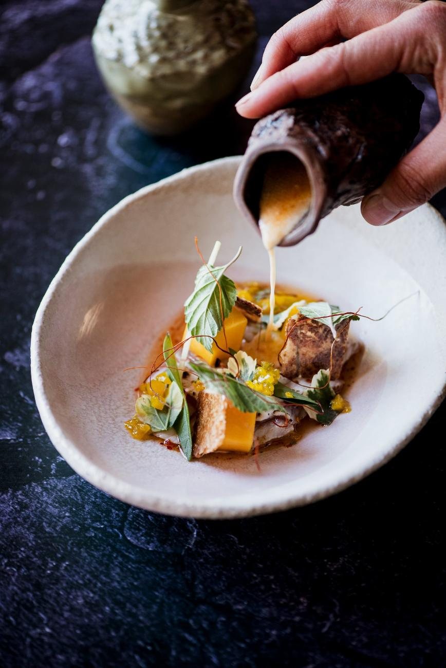 A sauce being poured over a plated dish