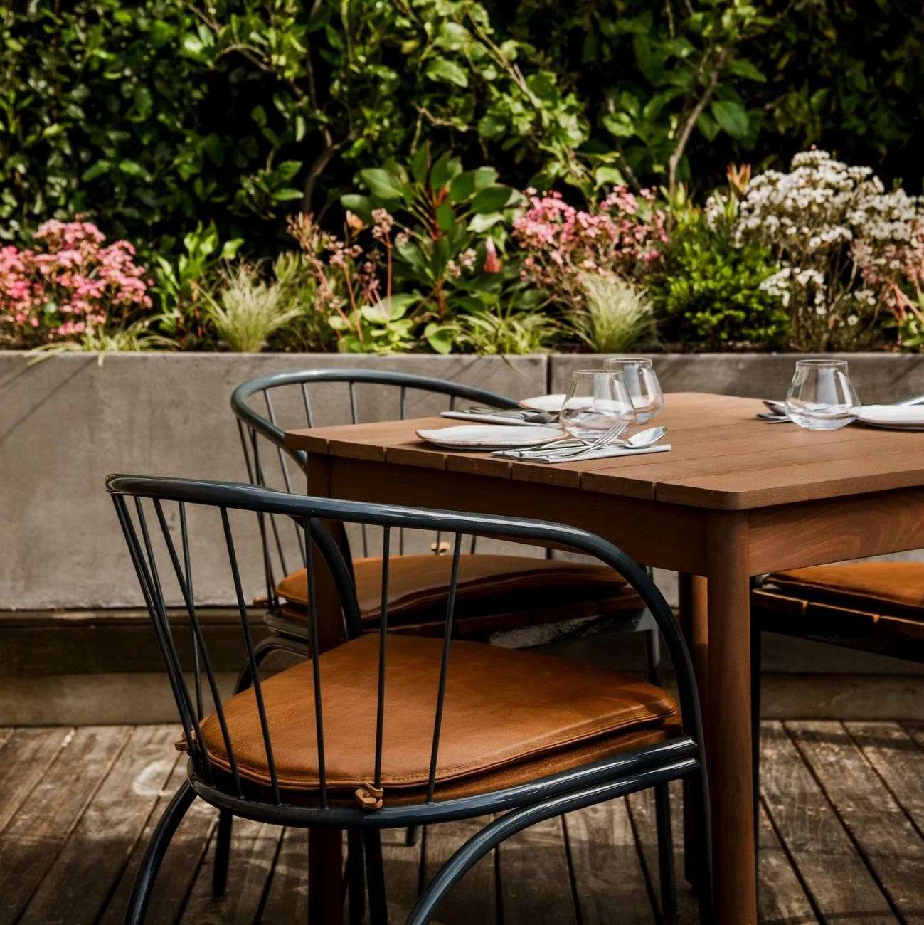 A wooden table on the terrace surrounded by flowers