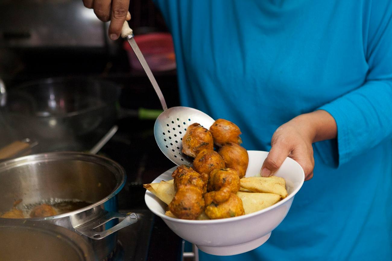 A cook lifting fried Cape Malay snacks from a pan