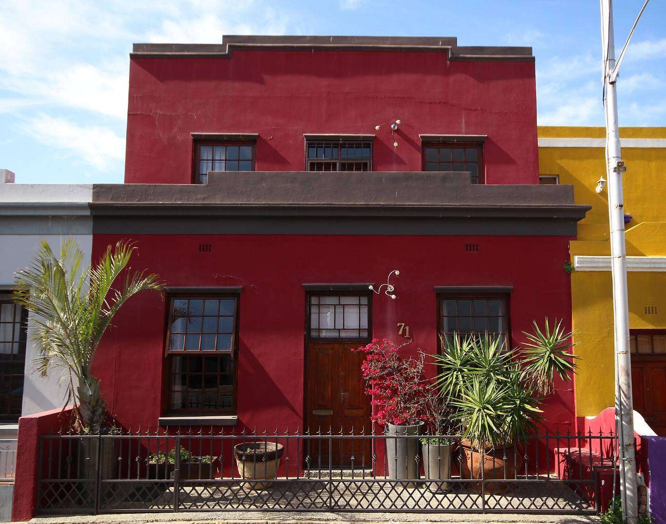 A deep red Bo-Kaap house with a balcony and pot plants