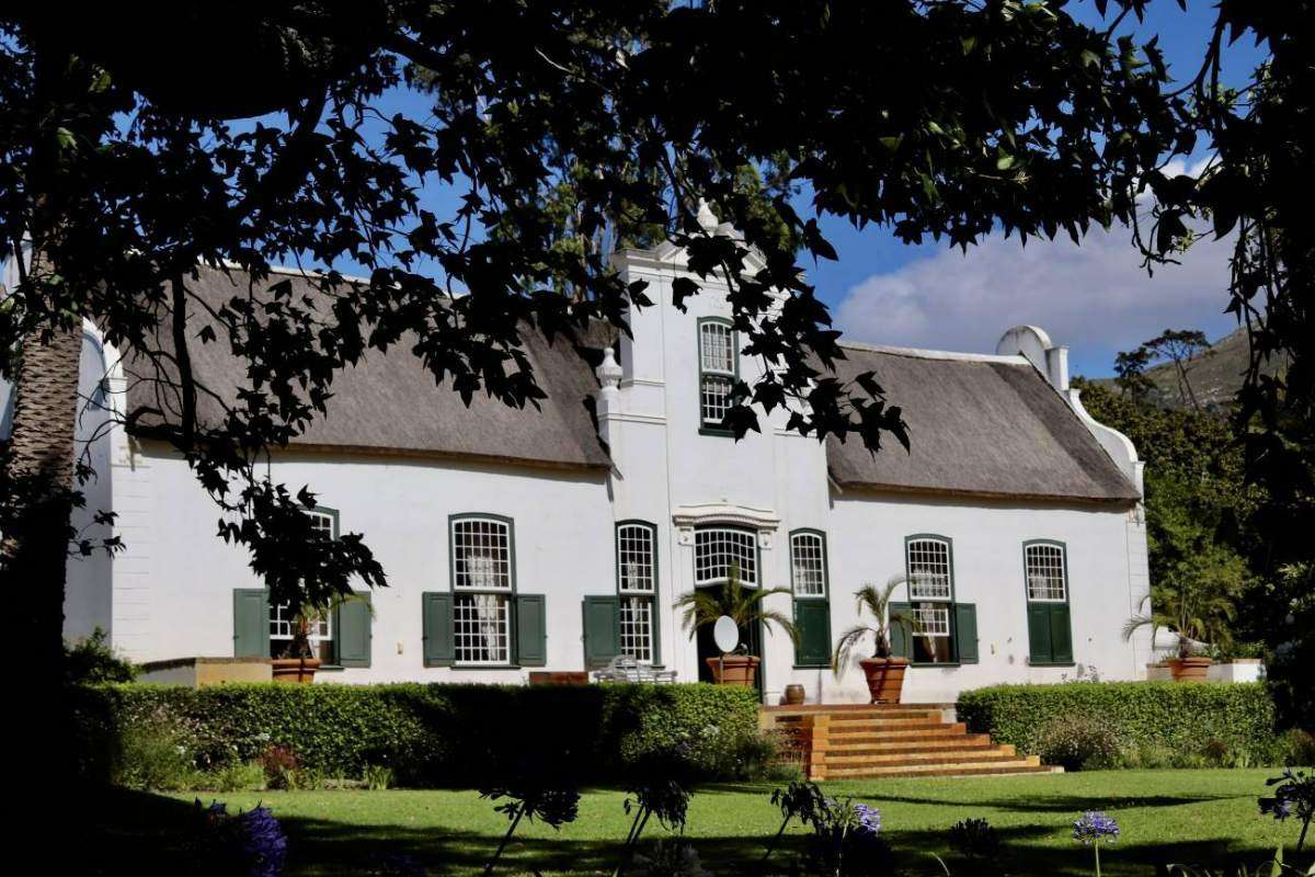 The white Cape Dutch manor house of Buitenverwachting behind trees and a lawn