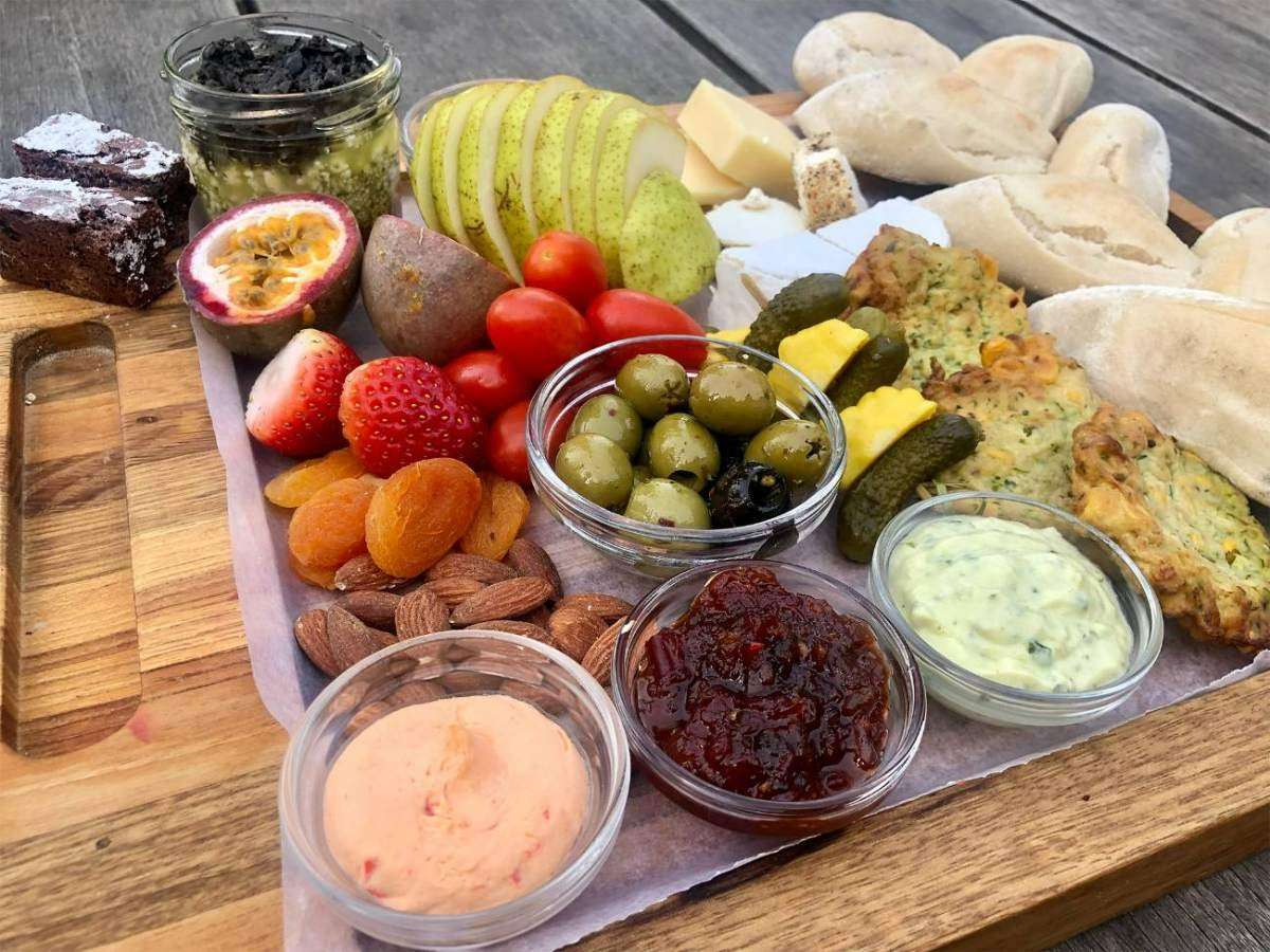 A wooden platter of cheese, fruit, olives and dips