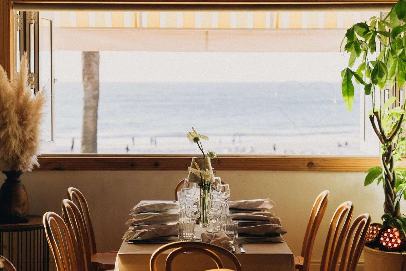 A table laid at the window, with Camps Bay beach and the Atlantic beyond