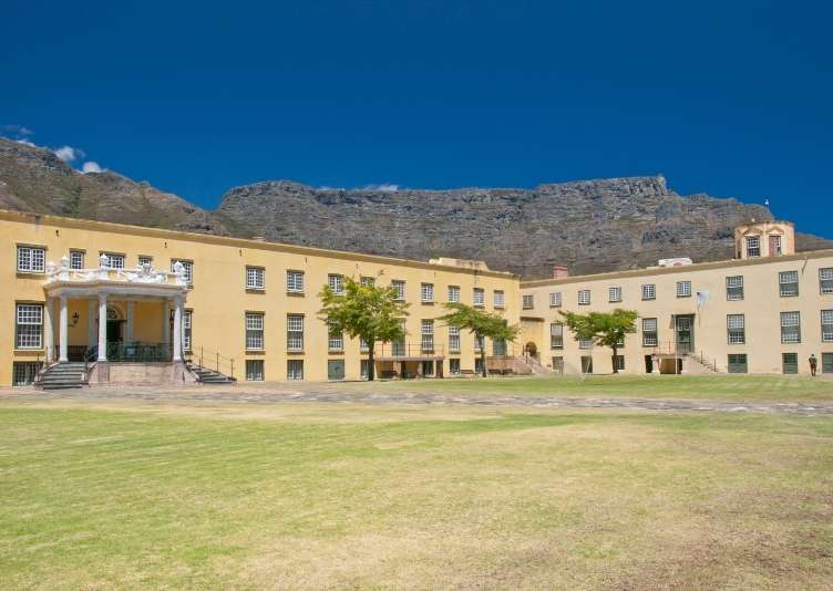 Yellow colonial buildings around a grassy courtyard with Table Mountain behind