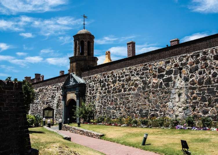 The arched stone entrance and bell tower of the Castle with flower beds in front