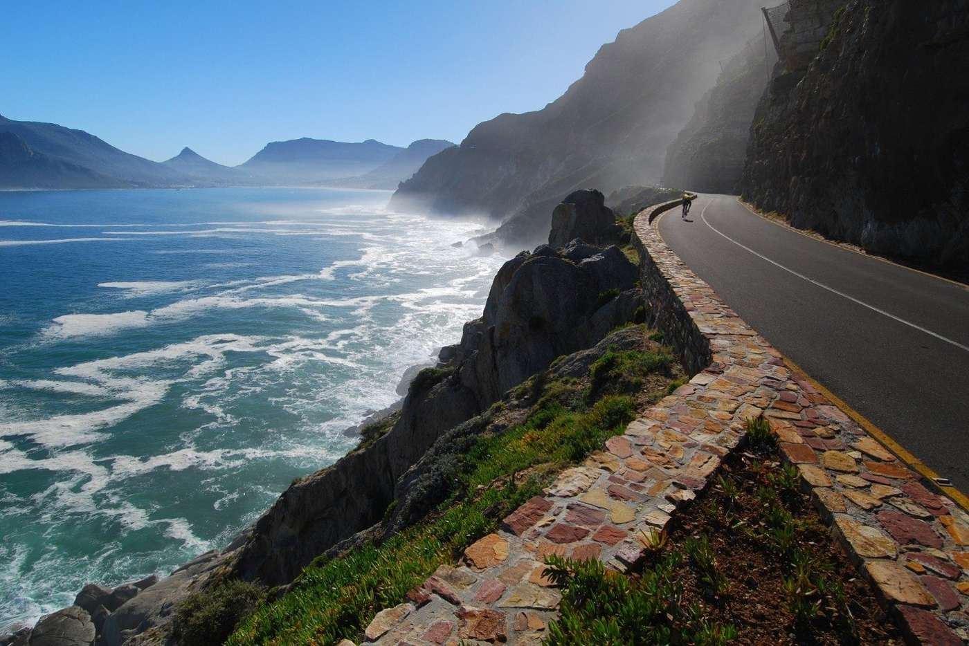 A cyclist on the road in sea mist, with Hout Bay beyond