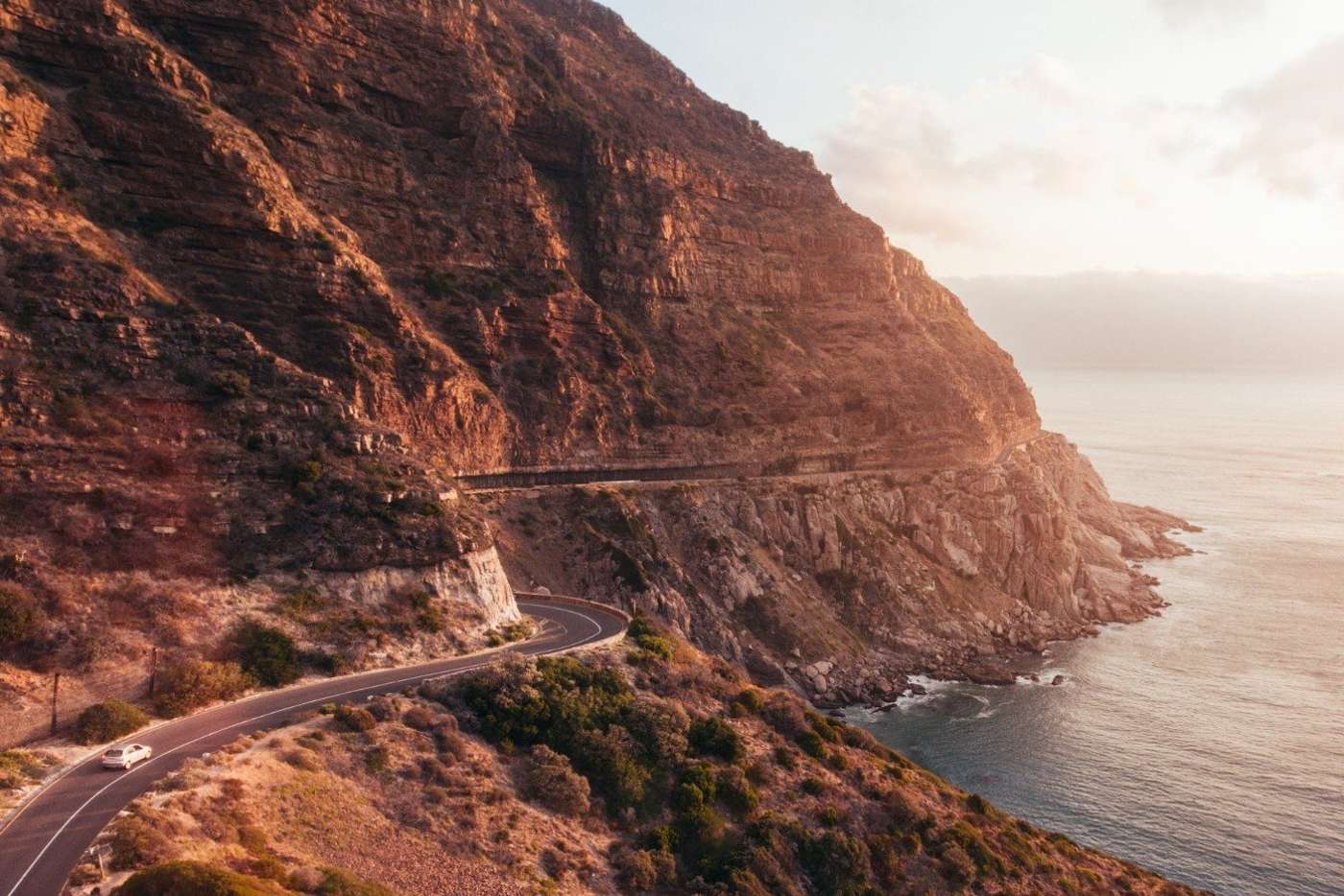 Chapman's Peak Drive at sunset, the road cut into red cliffs above the Atlantic, with a car on the bend
