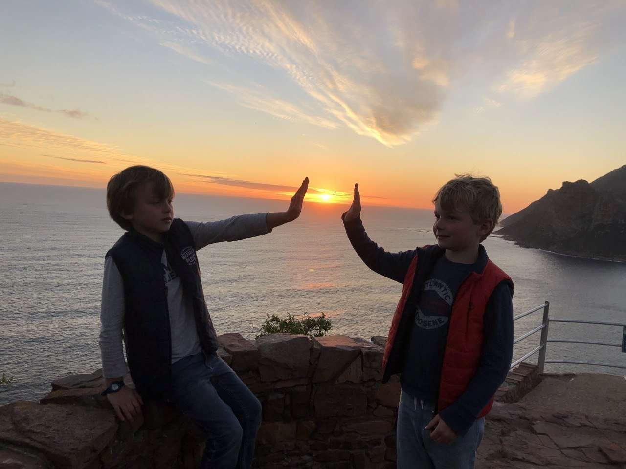 Two boys high-fiving against the sunset over the Atlantic
