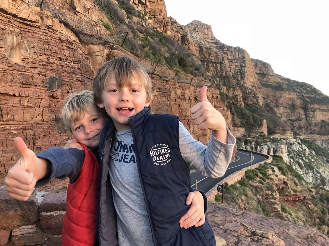 Two young boys giving a thumbs up at the lookout, with the cliffs and the road behind