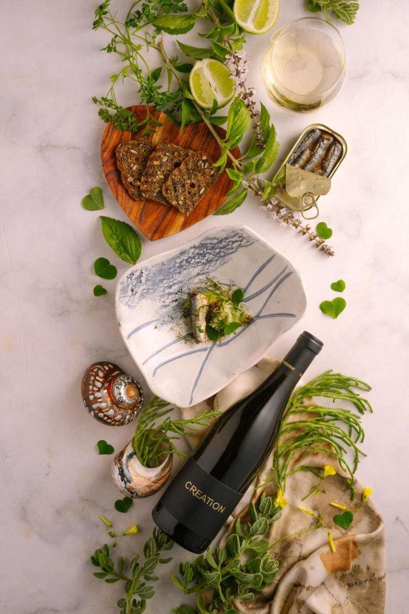 A plated course with herbs and flowers beside a bottle of Creation wine