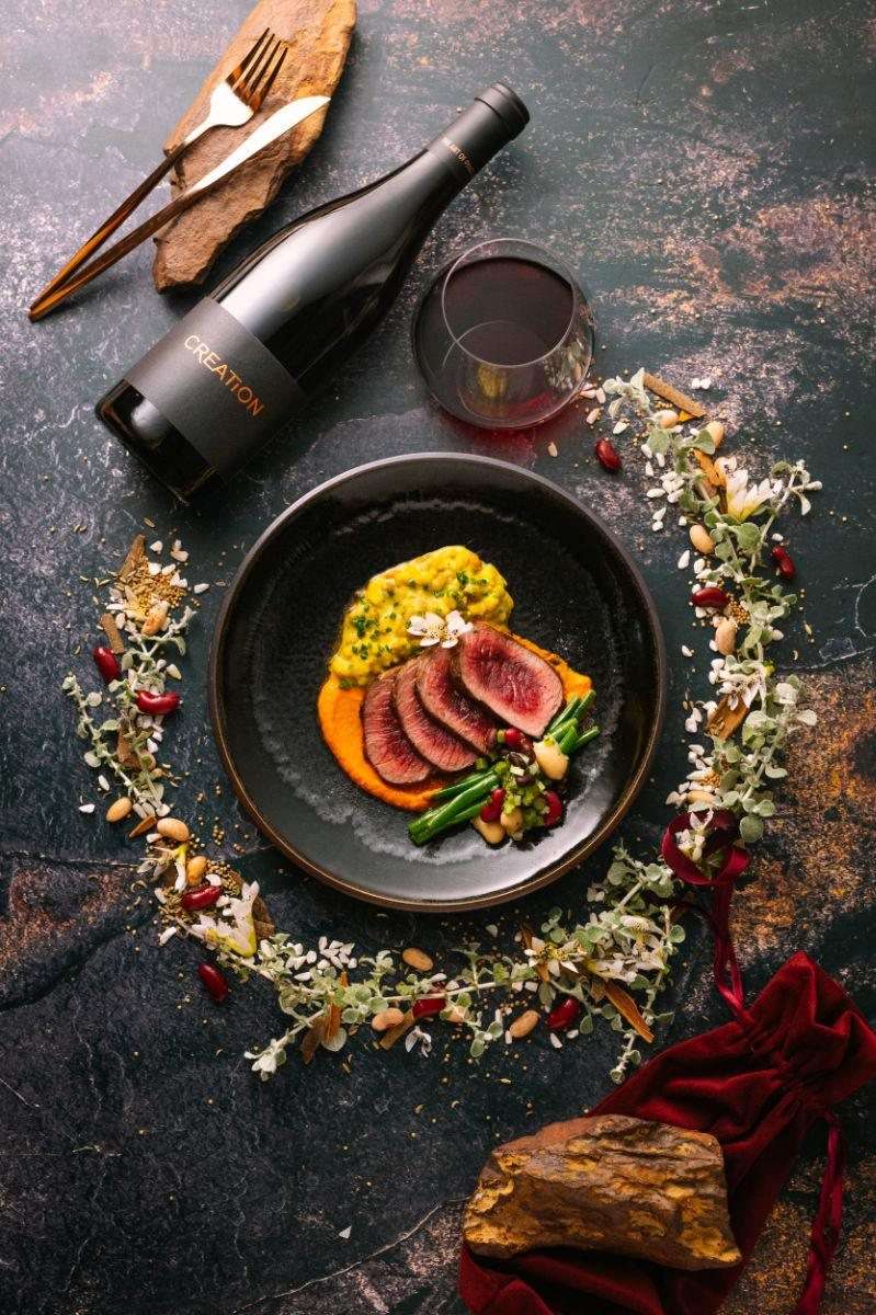 A dark plate with a course and a glass of red wine