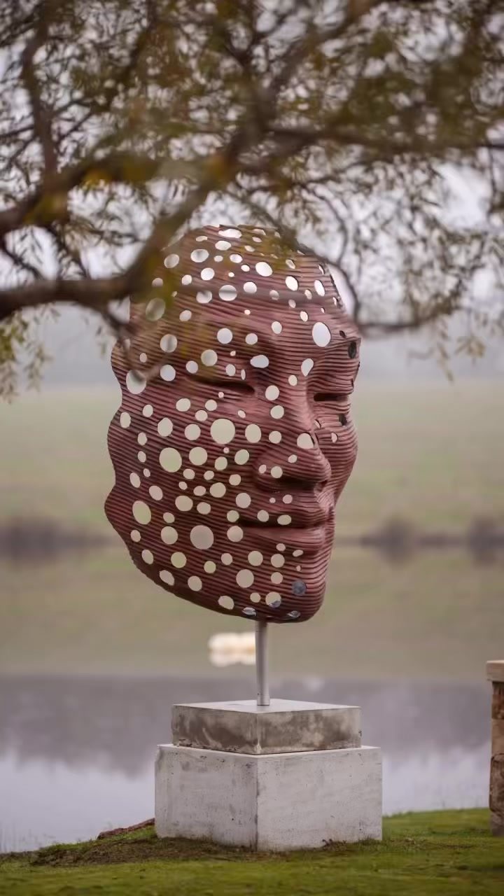 A large sculpted face covered in white dots, on a plinth above the dam