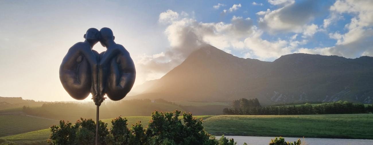 A bronze sculpture silhouetted against the sunset over the mountains