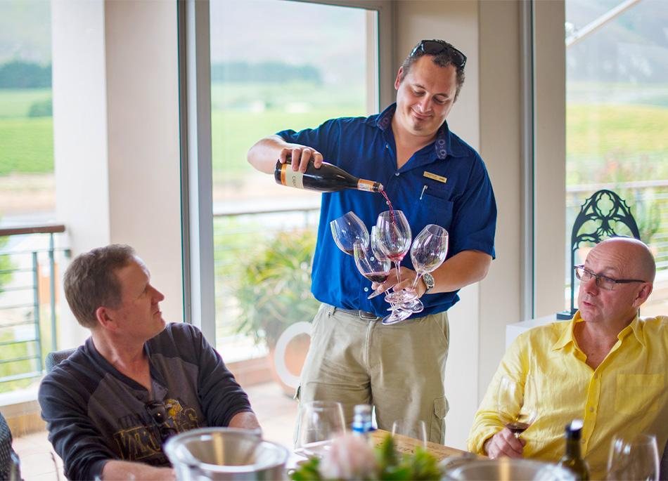 A host pouring wine for guests at a table by the window