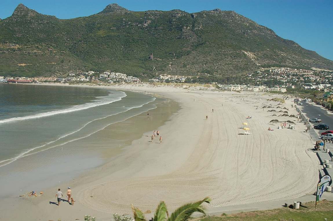 A wide sandy beach curving along Hout Bay with green mountains behind