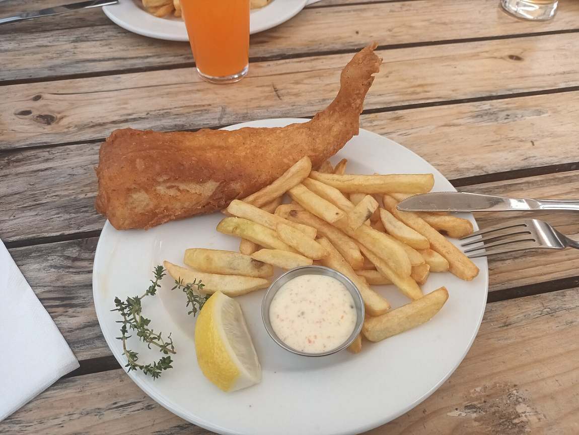 A plate of fried fish, chips and tartare sauce on a wooden table