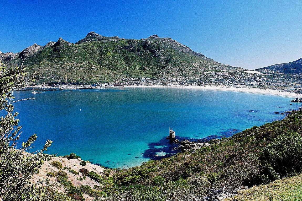 The turquoise curve of Hout Bay seen from Chapman&rsquo;s Peak Drive, the beach and the valley beyond
