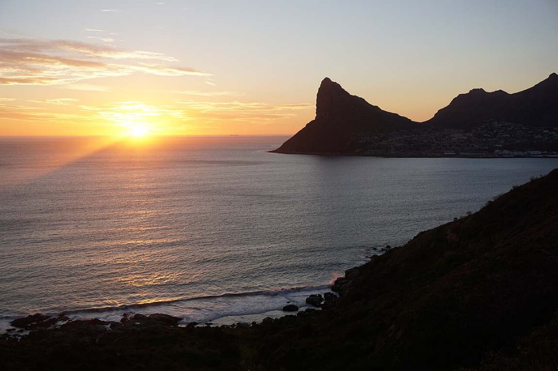 The sun setting over the sea beside the dark outline of the Sentinel