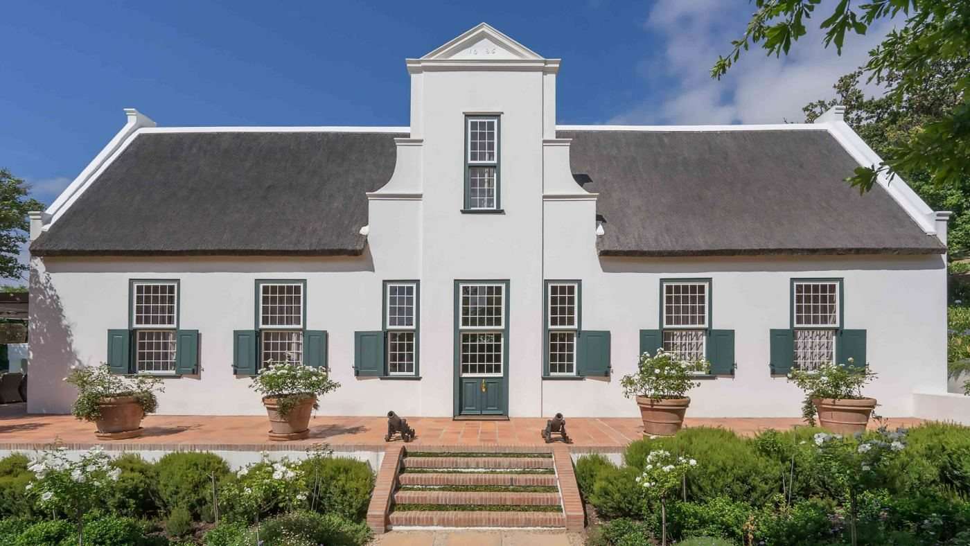 The white gabled Cape Dutch homestead of Klein Constantia with green shutters and a garden in front