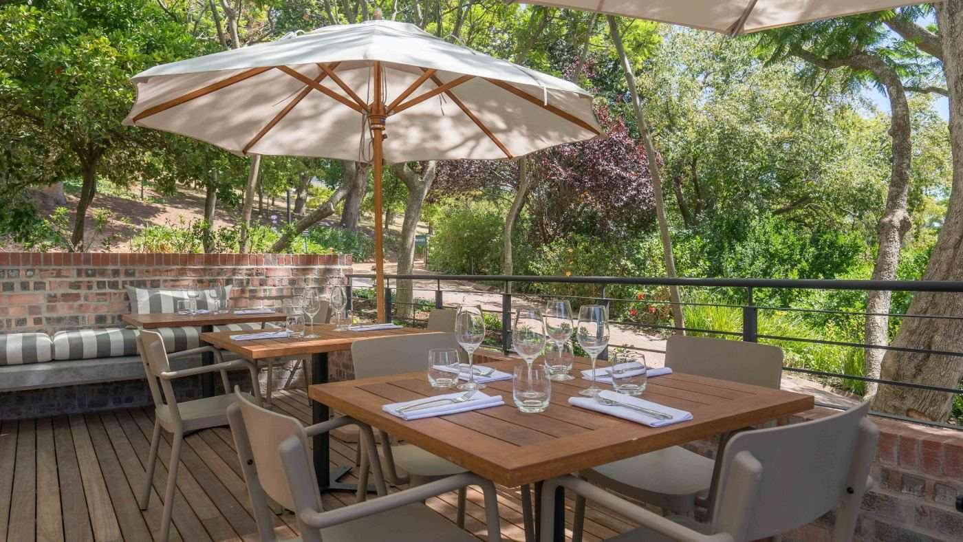 Tables and white umbrellas on a wooden terrace surrounded by trees