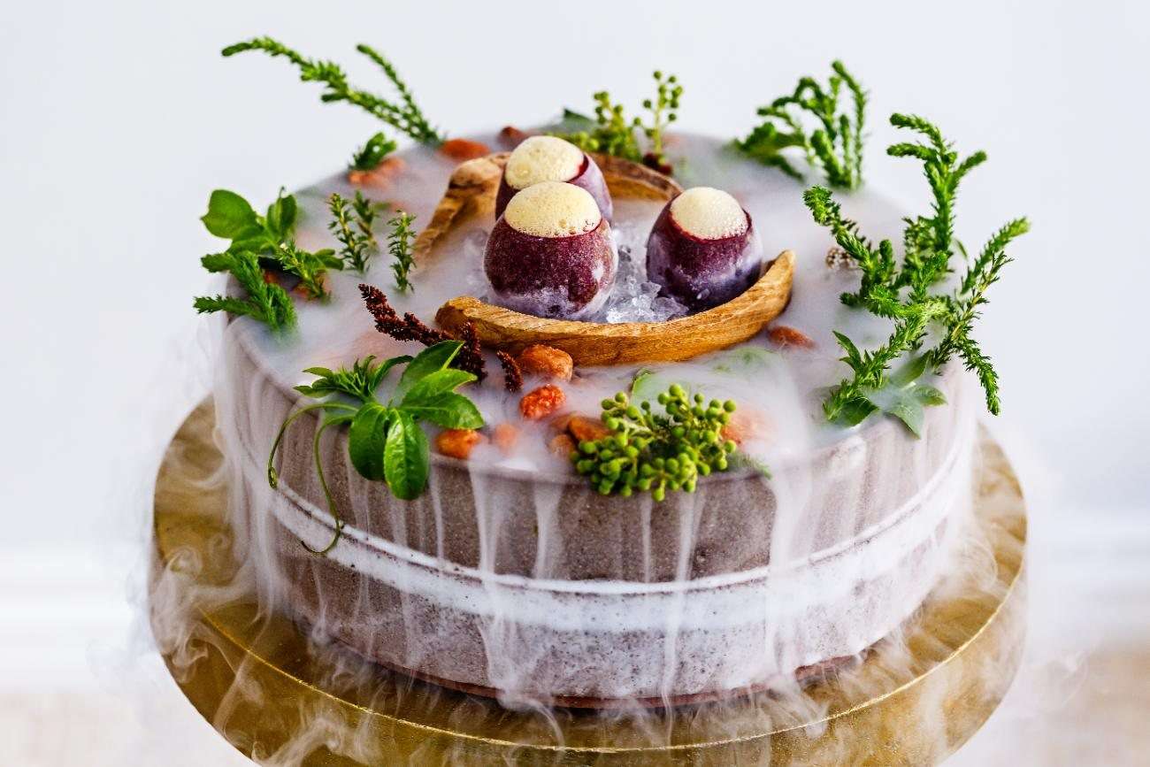 A course dressed with herbs and flowers on a raised plate