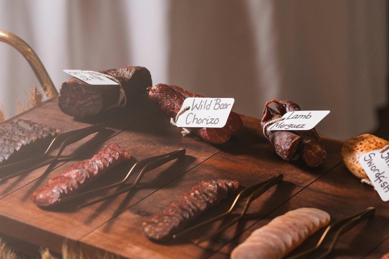 Cured meats on a wooden board in warm light, each labelled by hand