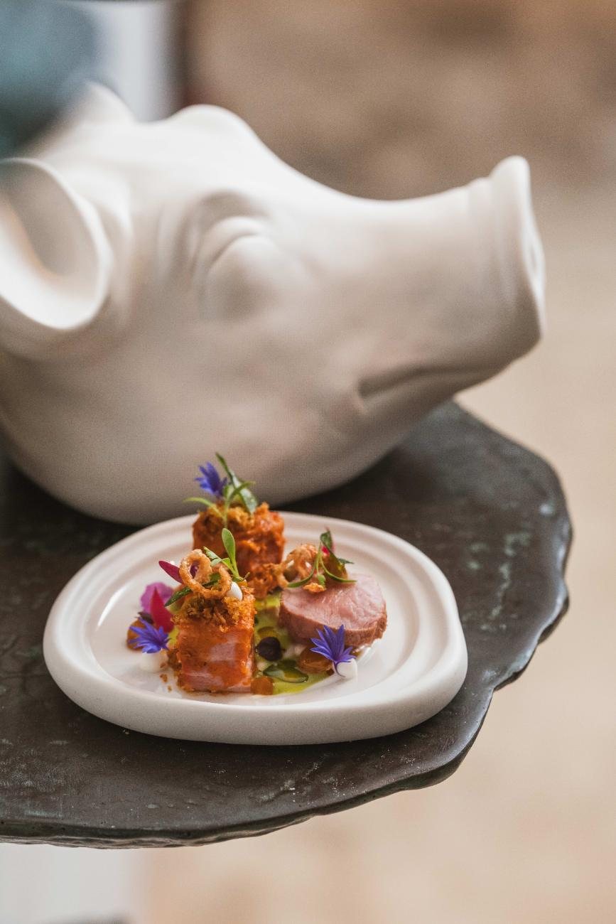 A white porcelain pig holding a plate with a small course