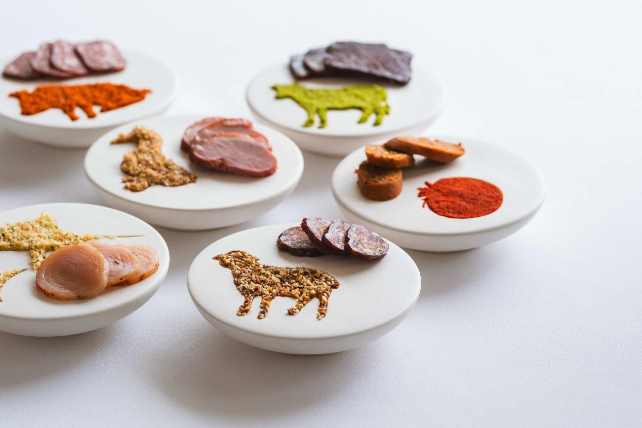 White plates with cured meats arranged in the shapes of animals