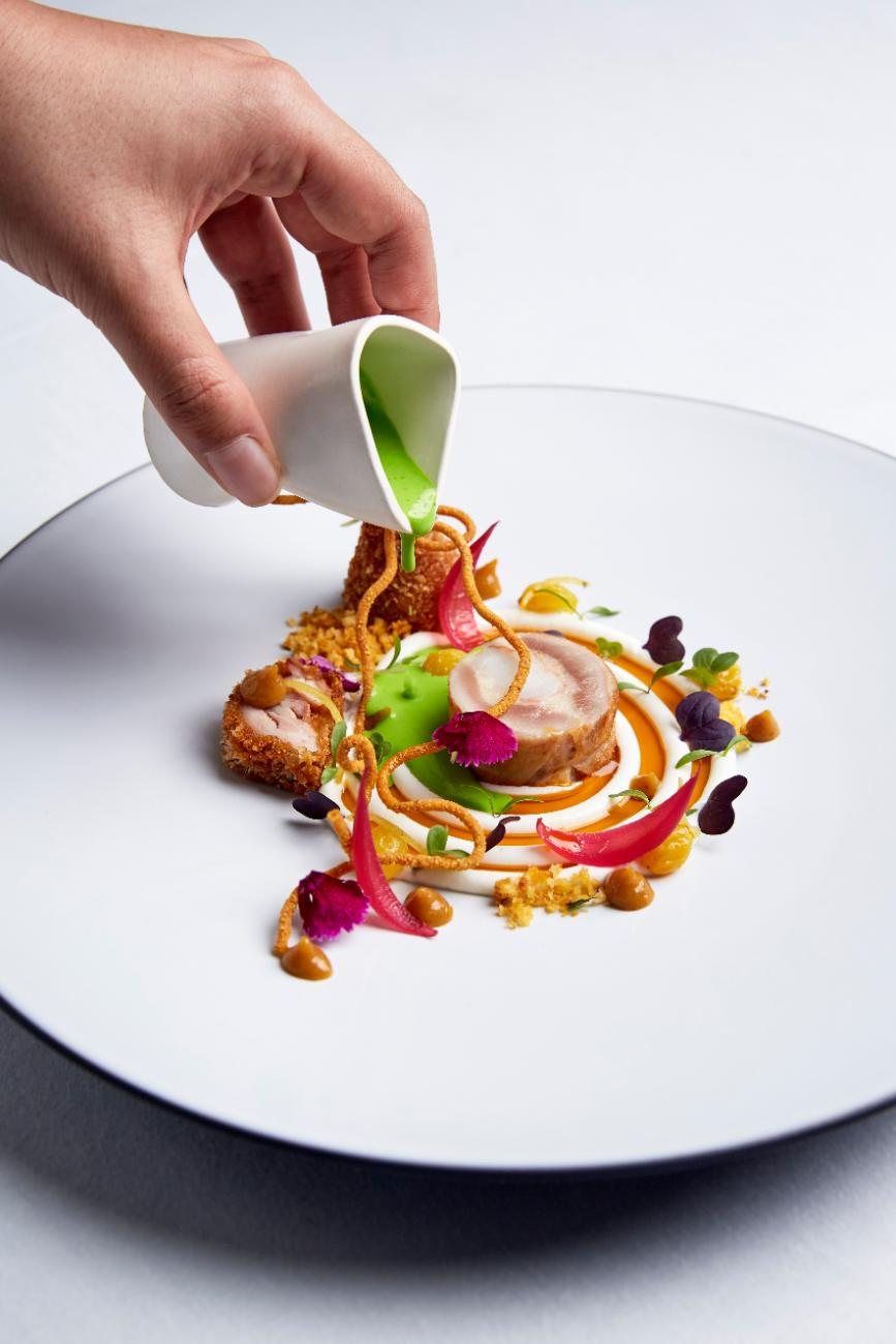 A hand pouring a green sauce onto a plated course