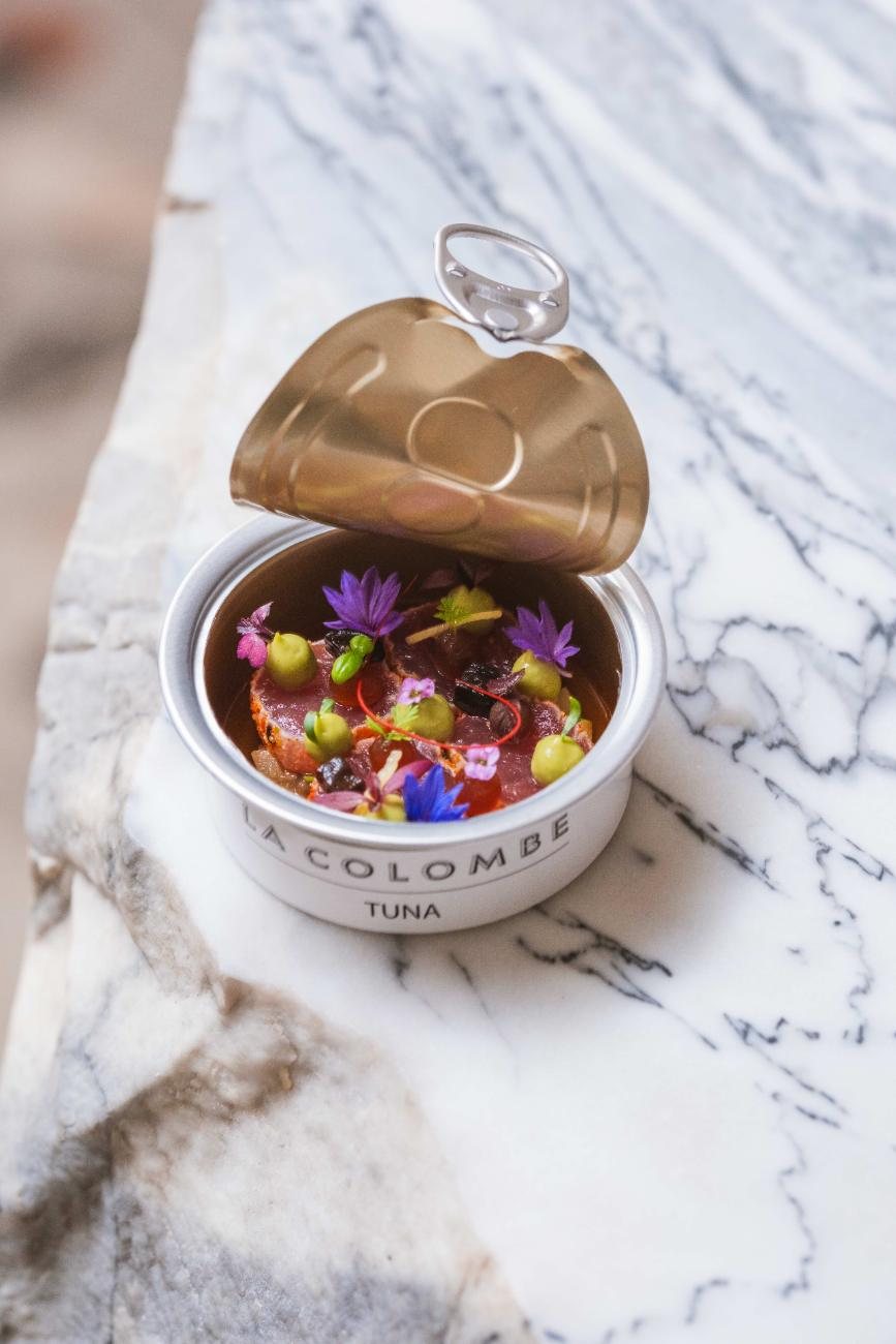 A small tin, opened, holding tuna with flowers and herbs, on marble