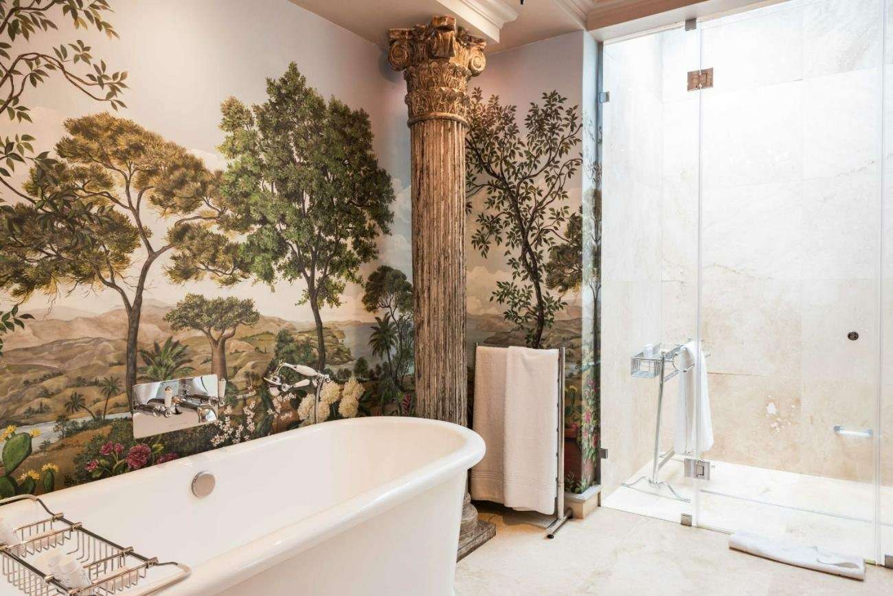 A bathroom with a free-standing bath and a painted landscape wall