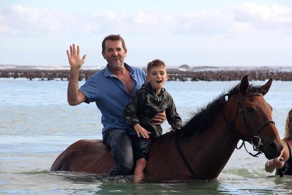 A father and son on a horse swimming in the sea