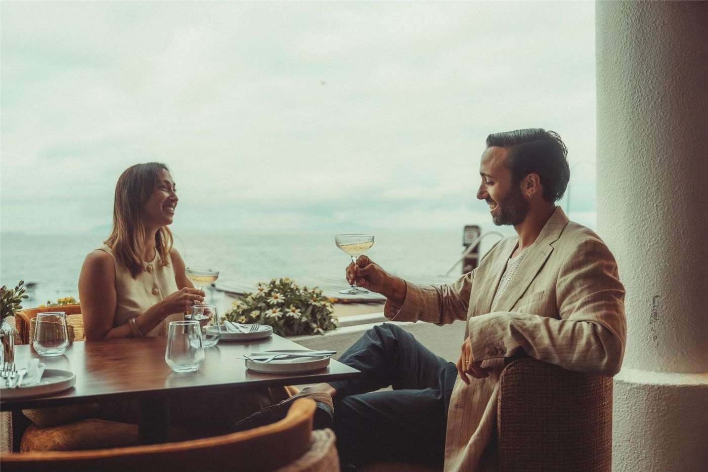 A couple with drinks by the water at sunset