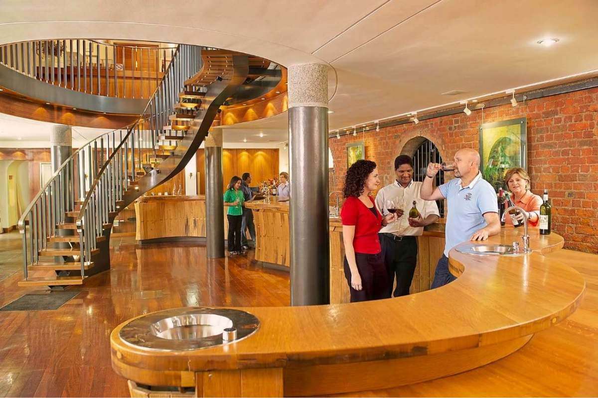 Guests at a curved wooden bar in a tasting room with a spiral staircase