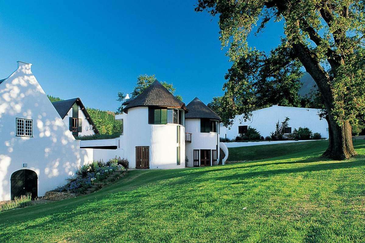 Whitewashed buildings with thatched roofs on green lawns under oak trees