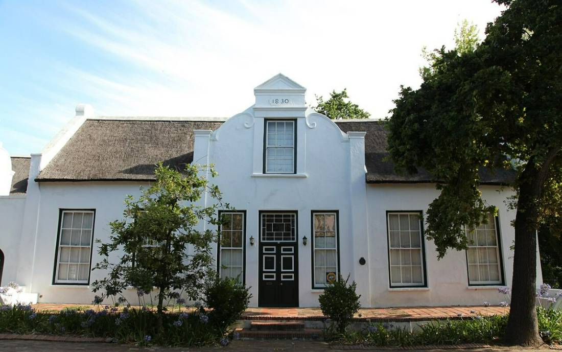 A white house with a curved Cape Dutch gable behind a low wall