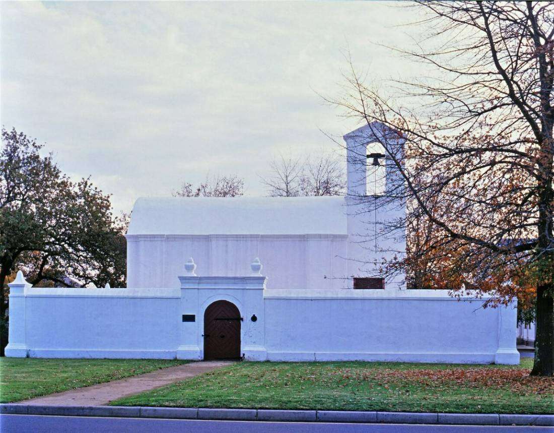 A small whitewashed building with a bell tower behind a low wall