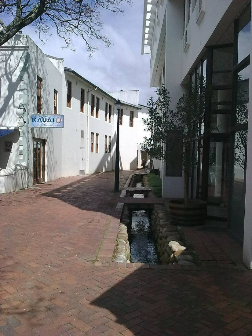 A narrow water furrow running along a brick pavement between white buildings
